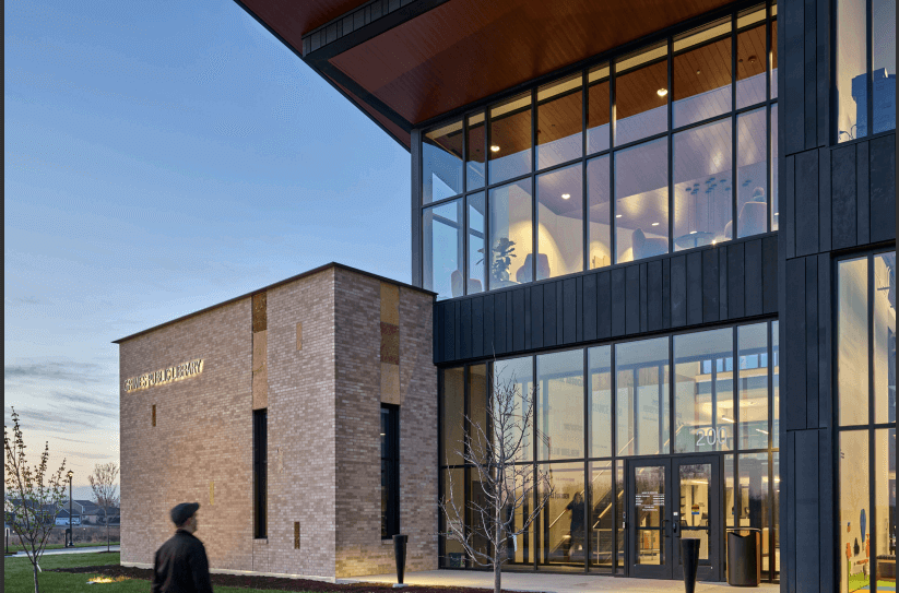Modern public library building with large glass windows, a brick wall section labeled “Grimes Public Library,”